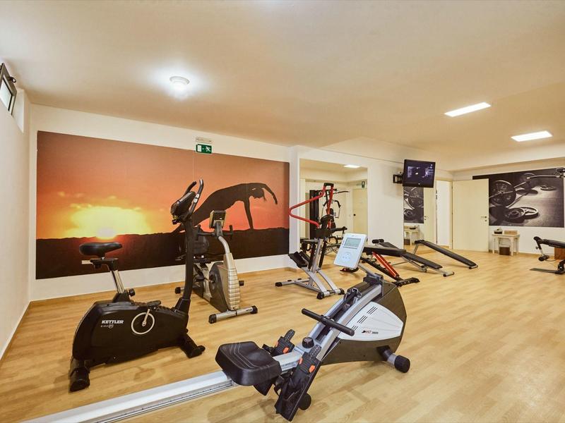 Gimnasio moderno con varios equipos de entrenamiento y una imagen de puesta de sol en la pared.