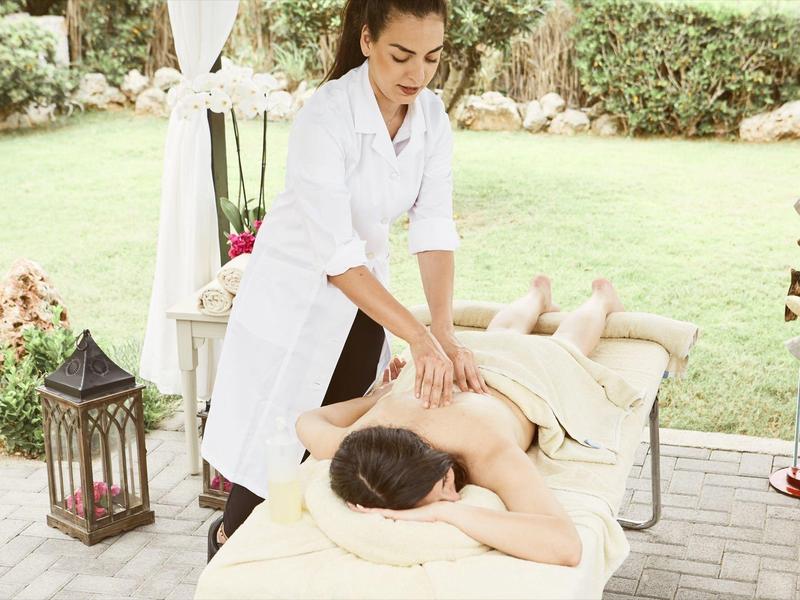 Mujer recibe masaje al aire libre en camilla, rodeada de jardín y decoración.