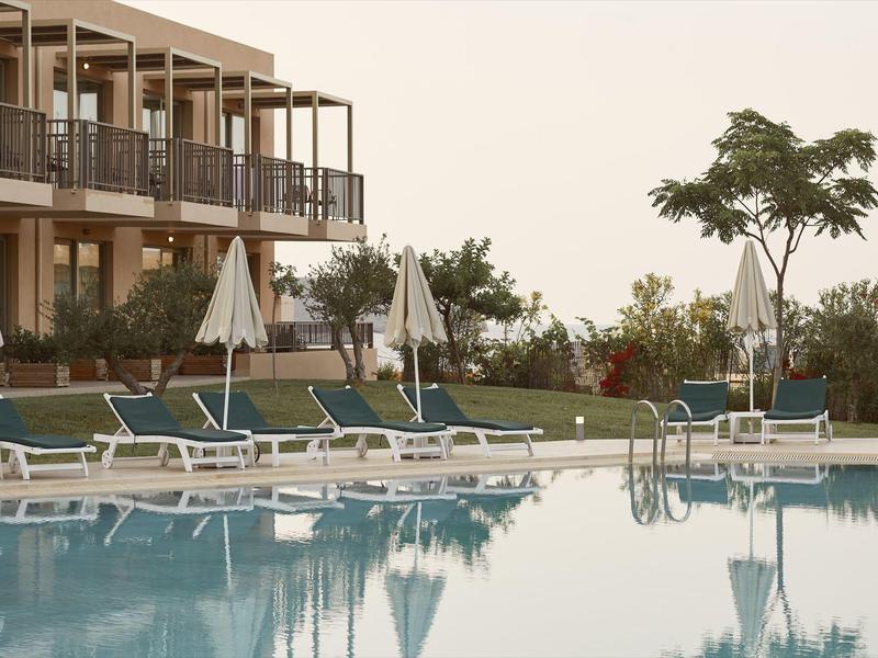 Piscina de hotel moderno con tumbonas, sombrillas y plantas en clima tranquilo al atardecer.