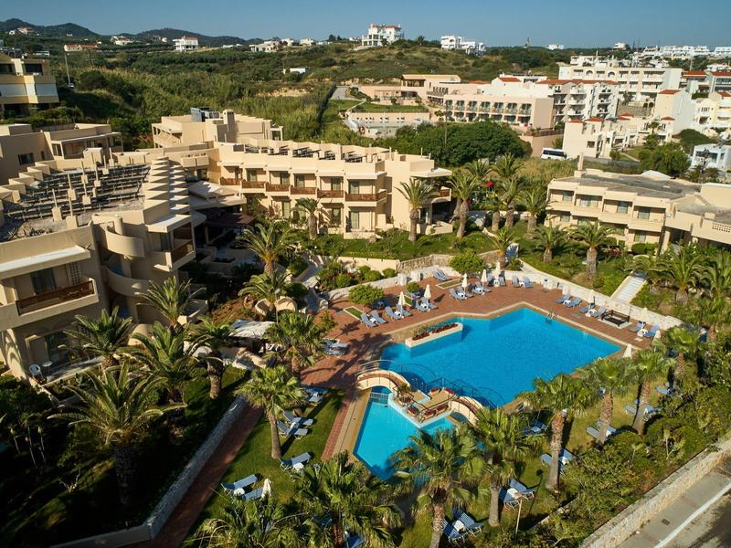 Gran complejo con varios edificios, piscina, palmeras y paisaje verde alrededor en la ladera.