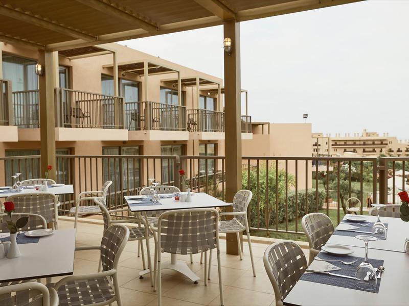 Terraza cubierta con mesas preparadas y vista a edificios del hotel y ciudad al fondo.
