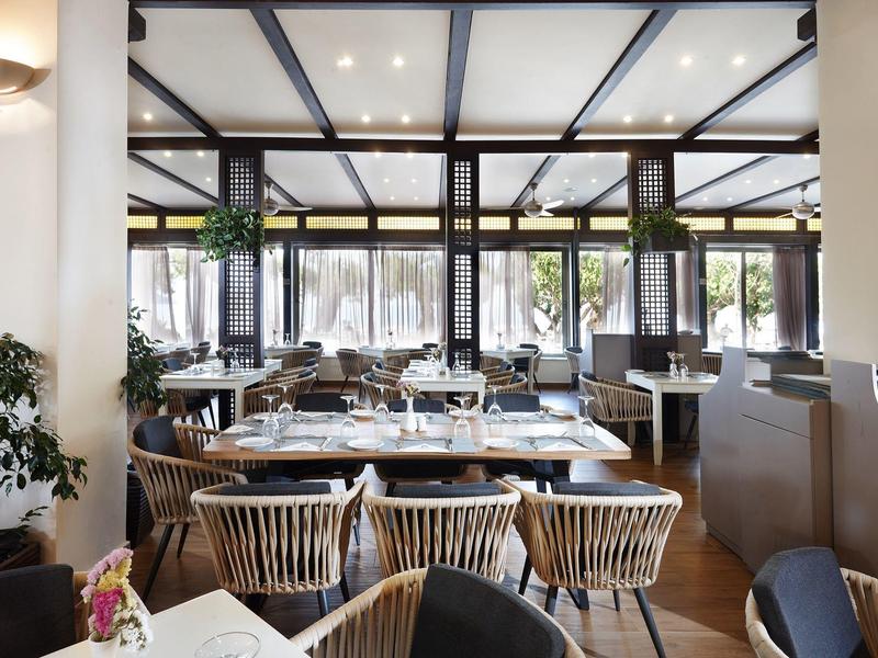 Restaurante luminoso con muebles modernos de madera y grandes ventanales con vista al exterior.