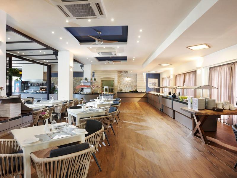 Restaurante moderno de hotel con suelo de madera, sillas blancas y mesas espaciosas junto a las ventanas.