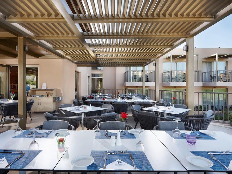 Restaurante al aire libre con mesas preparadas, asientos y vista a balcones del hotel.