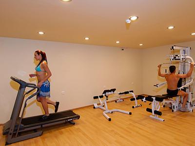 Osoby ćwiczące na bieżni i maszynie siłowej w małej sali fitness.