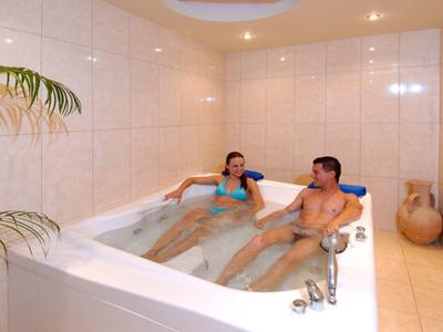 Stel ontspant in een groot bubbelbad in een lichte wellnessruimte.