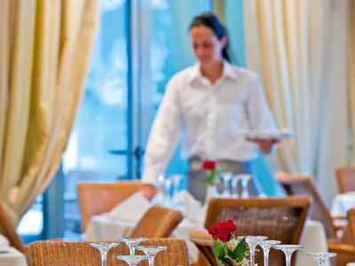 Tafel gedekt met glazen en servetten in een hotelrestaurant met een serveerster op de achtergrond.