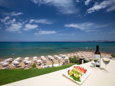 Blick auf Meer mit blauem Himmel, weißen Sonnenschirmen am Strand und Salat mit Wein auf Balkon.
