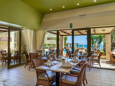 Helles Restaurant mit gemütlichen Holztischen und Blick auf sonnige Terrasse mit Palmen.