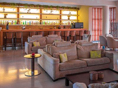 Moderne Bar mit braunen Sofas, Holztheke, hohen Stühlen und großen Fenstern mit rotem Vorhang.