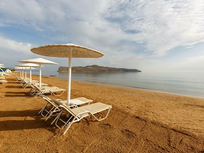 Leerer Sandstrand mit weiße Liegestühle und Sonnenschirme, ruhiges Meer und bewölkter Himmel.