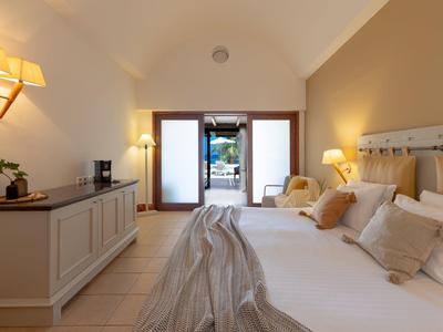 Hell eingerichtetes Schlafzimmer mit großem Bett, TV, zwei Sesseln und Zugang zum Garten.