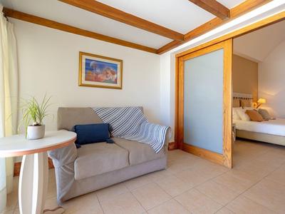 Hell eingerichtetes Wohnzimmer mit grauem Sofa, rundem weißen Tisch und Blick ins Schlafzimmer.