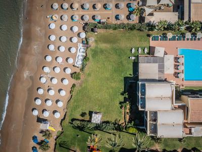 Luftaufnahme eines Hotels mit Pool, Liegestühlen und Sonnenschirmen am Strand.
