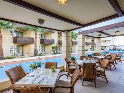 Überdachte Terrasse mit Essbereich neben einem Hotelpool und Blick auf Hotelbalkone.