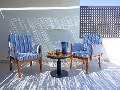 Zwei Stühle mit blauen Kissen und ein kleiner Tisch auf einer sonnigen Terrasse mit Schattenmuster.