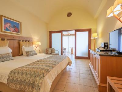 Helles Hotelzimmer mit Doppelbett, Nachttischlampen, Schreibtisch und Zugang zu einem Balkon.