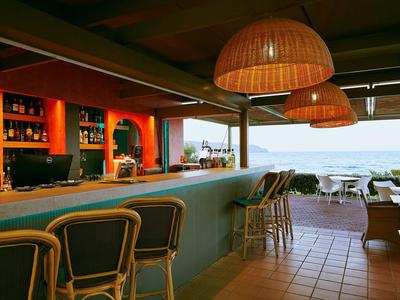 Offene Hotelbar mit Korblampen und Blick auf das Meer bei Dämmerung.
