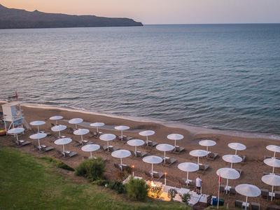 Strand mit weißen Sonnenschirmen und Stühlen vor ruhigem Meer bei Sonnenuntergang.