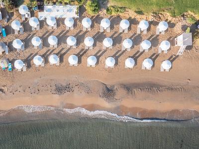 Luftaufnahme eines Strandes mit Reihen von weißen Sonnenschirmen und sandigem Ufer am Wasser.