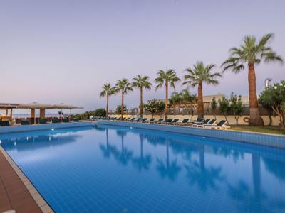 Großer Pool mit klarem Wasser und Palmen am Rand bei ruhiger Hotelumgebung.