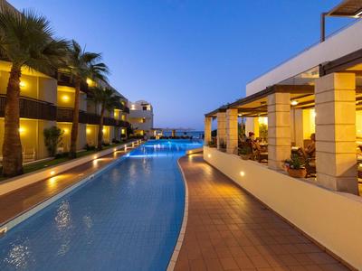 Ein beleuchteter Hotelpool mit Palmen und Gebäude bei Dämmerung.