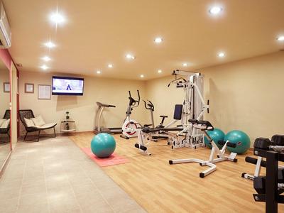 Moderner Fitnessraum mit Trainingsgeräten, Gymnastikbällen und Spiegelwand in hellem Raum.