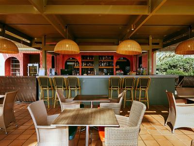 Moderne Hotelbar mit Holz- und Rattanmöbeln, drei Hockern und indirekter Beleuchtung.