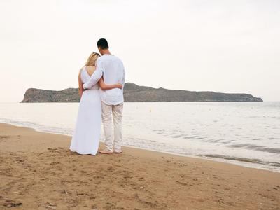 Ein Paar umarmt sich am Strand mit Blick auf das Meer und eine Insel im Hintergrund.