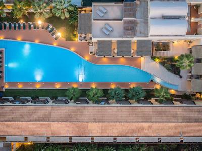 Ein beleuchteter Pool in Gitarrenform mit Liegestühlen und Pflanzen in einem Hotel.