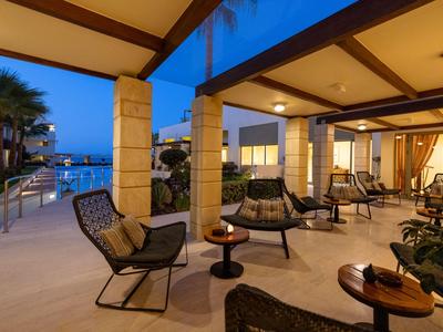 Offener Lounge-Bereich in einem Hotel mit Sesseln, Tischen und Blick auf einen Pool bei Abendlicht.