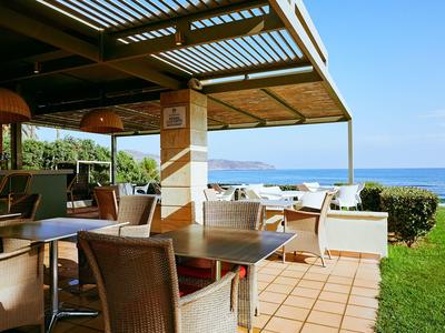 Offene Terrasse eines Hotels mit Tischen, Stühlen und Blick auf das Meer und den Garten.