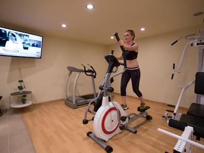 Frau trainiert auf einem Heimtrainer in einem modernen, gut beleuchteten Fitnessraum.