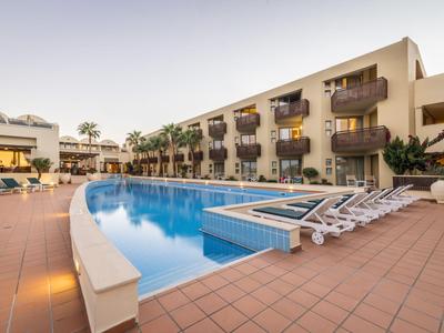 Moderner Hotelpool mit Sonnenliegen und Balkonen an den Zimmern im Hintergrund.