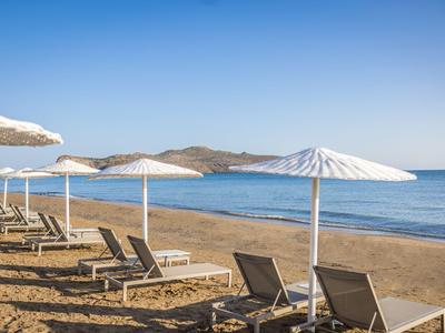 Leerstehende Liegestühle unter weißen Sonnenschirmen am ruhigen Sandstrand mit Blick auf das Meer.