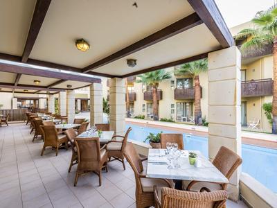Überdachte Terrasse mit Tischen und Stühlen neben einem Pool in einem Hotel.
