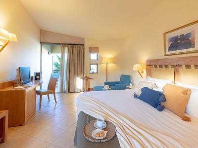 Helles Hotelzimmer mit großem Bett, Sitzbereich, Schreibtisch und Blick auf Balkon.