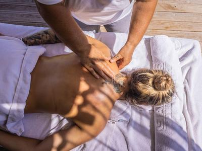 Eine Person erhält eine Rückenmassage auf einer weißen Liege, Außenbereich mit Holzboden.