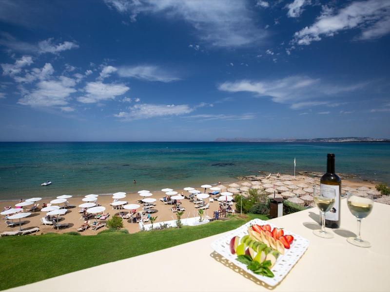Zeezicht met ligbedden op het strand, een fles wijn, glas en bord met eten op een balkon.