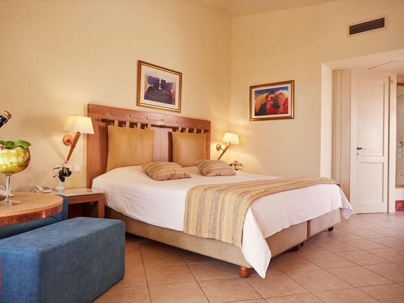 Gezellige hotelkamer met tweepersoonsbed, nachtlampjes, schilderijen en zithoek met tafel en poefs.