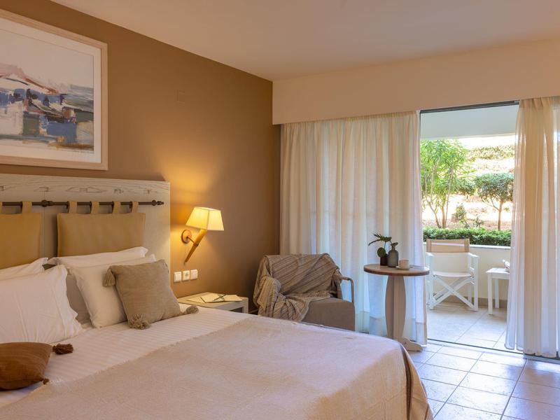 Gezellige hotelkamer met bed, fauteuil, tafel en schuifdeur naar terras.