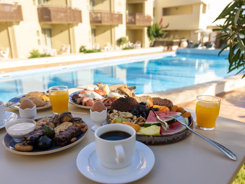 Ontbijt met koffie, sap en gebak bij een zonnig zwembad.