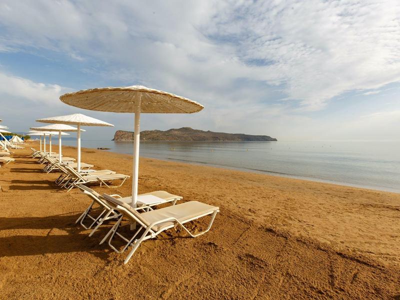 Lege strandstoelen en parasols op een zandstrand met kalme zee en mistige lucht.