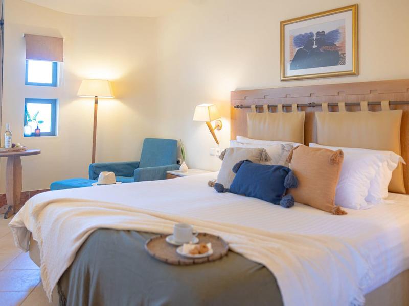 Gezellige hotelkamer met groot bed, zachte kussens, fauteuil en warme verlichting.