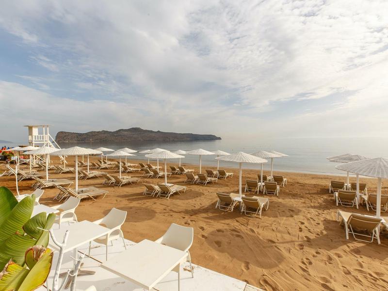 Zandstrand met witte parasols en stoelen onder een deels bewolkte lucht bij de zee.