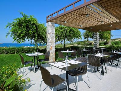 Restauracja na świeżym powietrzu z stołami, krzesłami i widokiem na morze pod zadaszeniem.