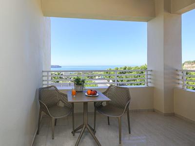 Balkon mit Tisch und zwei Stühlen mit Meerblick und Obstkorb.
