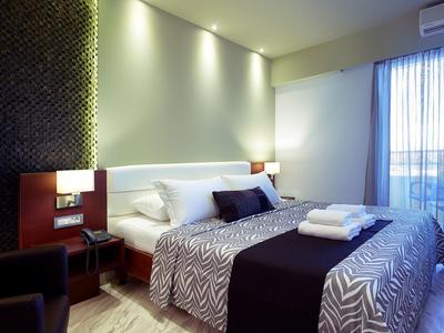 Modern hotelkamer met tweepersoonsbed, nachtkastjes, leeslampen en balkon met gordijn.