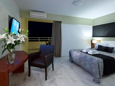 Moderne hotelkamer met tweepersoonsbed, stoel, tafel met bloemen en tv.