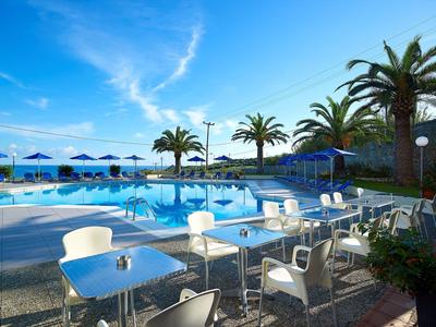 Moderner Poolbereich mit weißen Stühlen, blauen Sonnenschirmen und Palmen bei klarem Himmel.